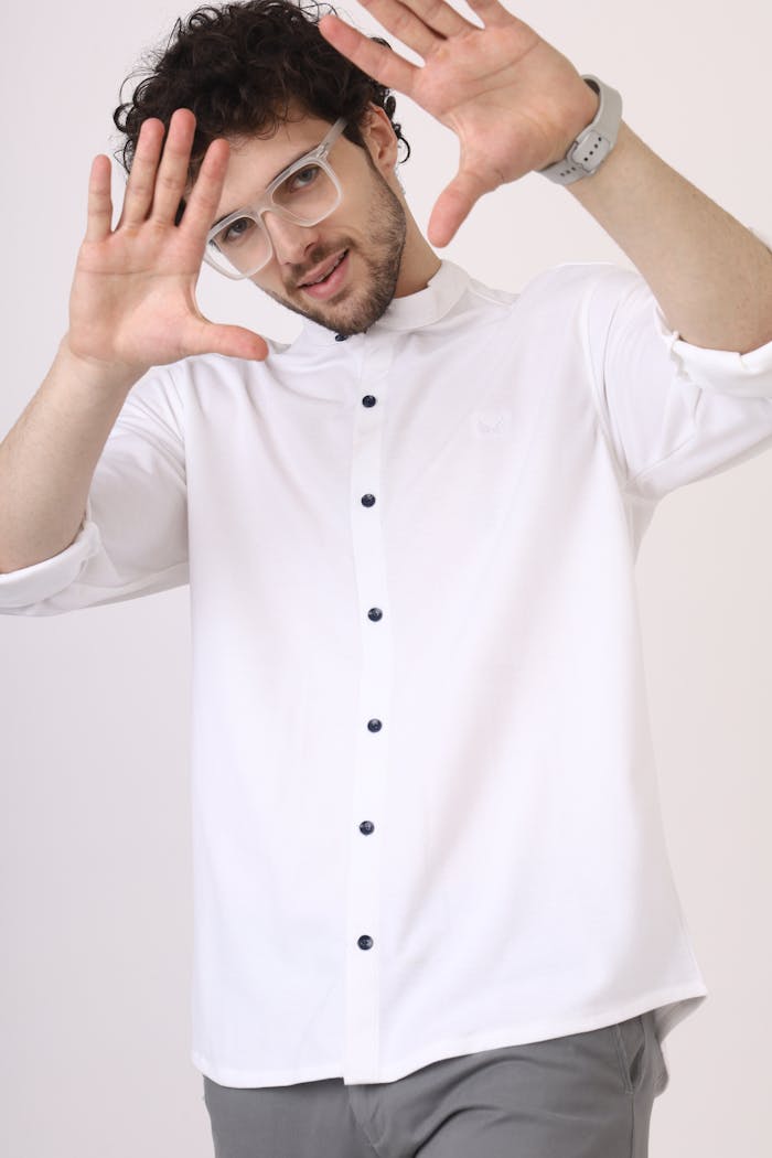 services-03 Young man in glasses poses playfully in white shirt, light background.