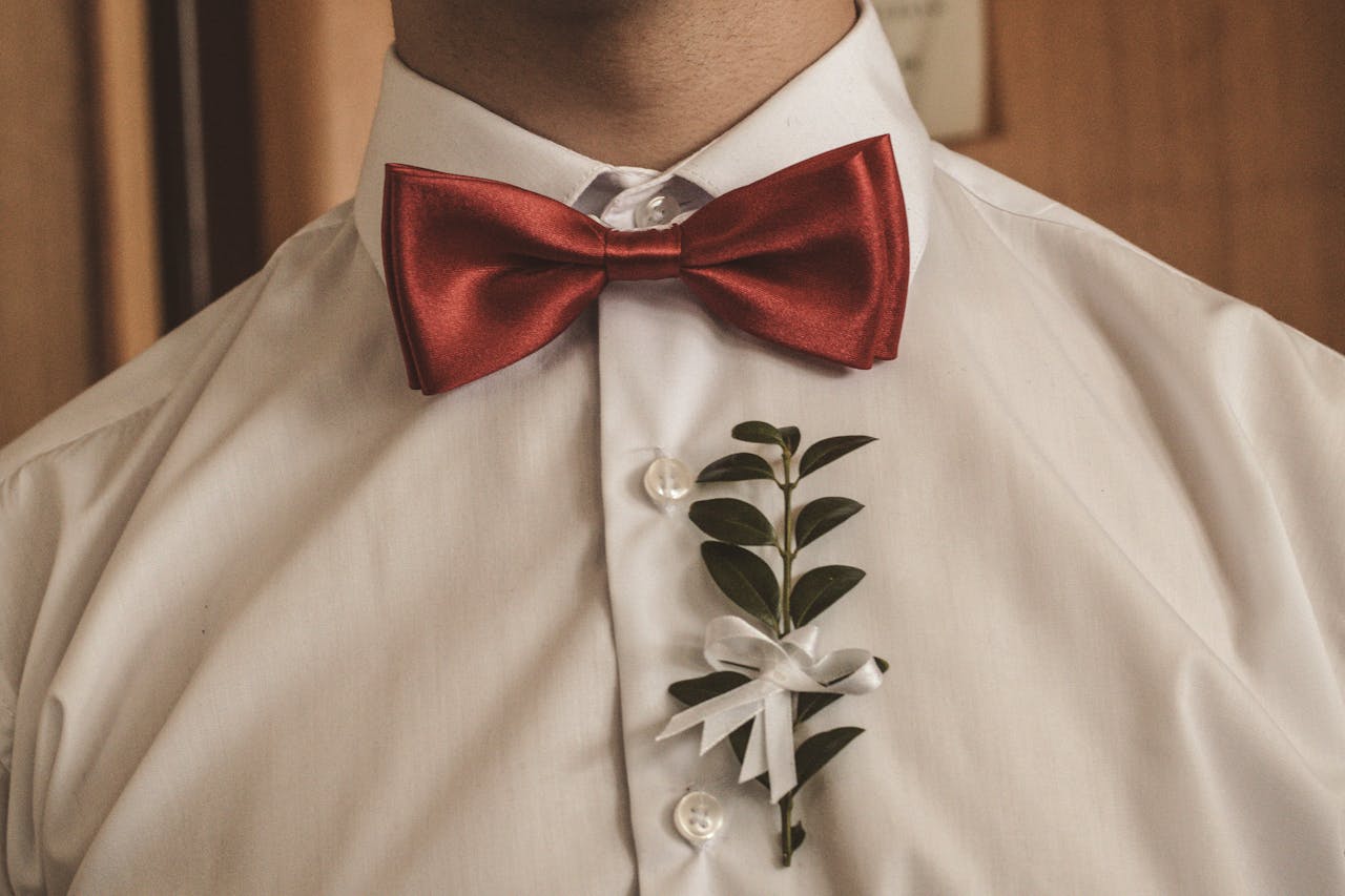 about-us Close-up of a red bow tie and boutonniere on a formal white shirt, exuding elegance.
