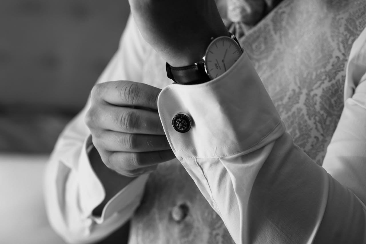 our-story Stylish black and white photo of a man adjusting his cufflinks, highlighting elegance and sophistication.