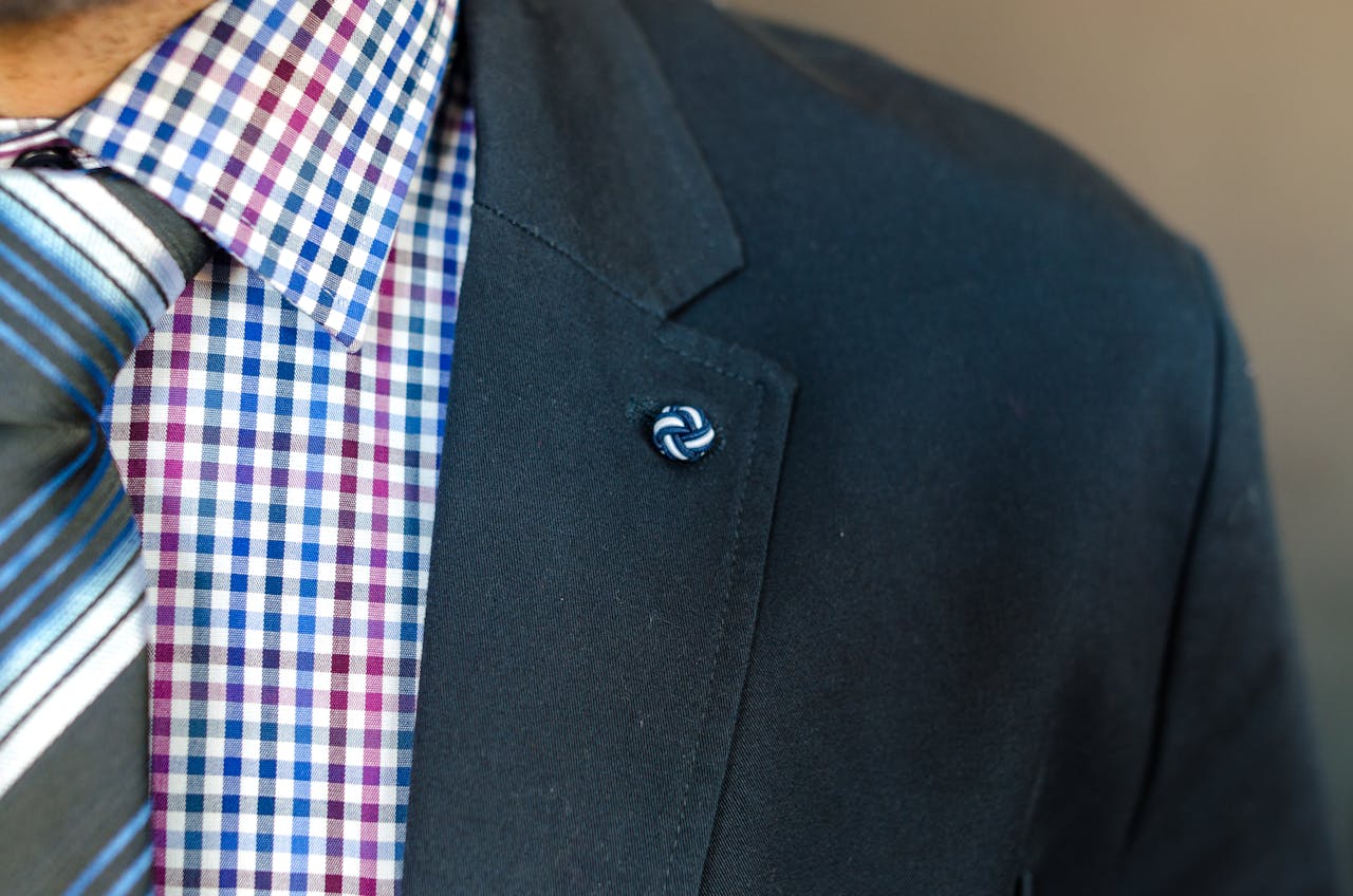 who-we-are Detailed close-up of a man's checkered shirt, suit jacket, and striped tie.