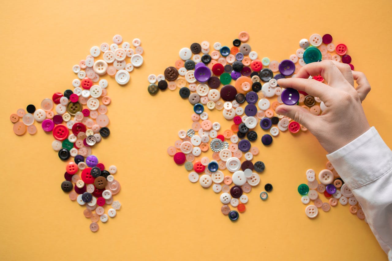 services-02 Hand arranging colorful buttons to form a world map on a vibrant yellow background.